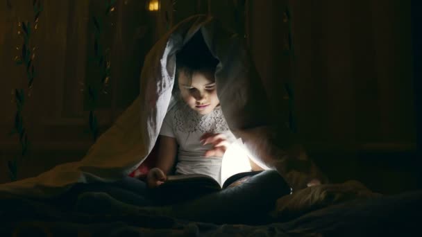 Dziewczyna czytanie książki z latarką pod okładek w nocy - Materiał filmowy, wideo