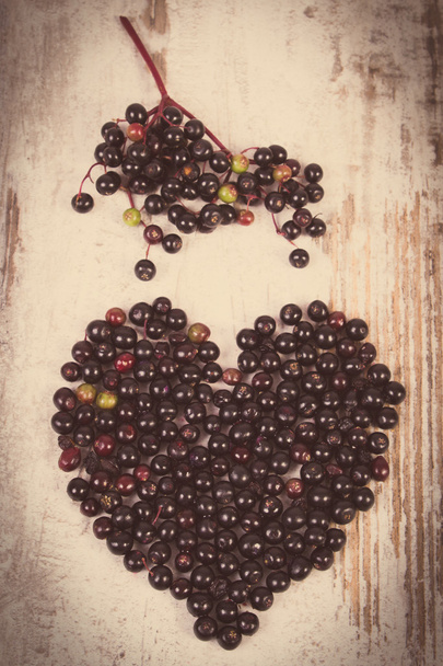 Vintage photo, Heart of fresh elderberry on old wooden background, symbol of love - Foto, immagini