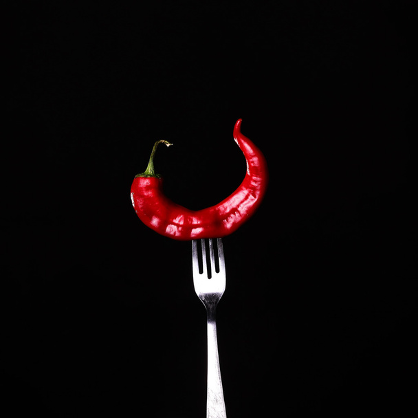 Tenedor empalado a chile rojo picante sobre fondo negro
. - Foto, Imagen