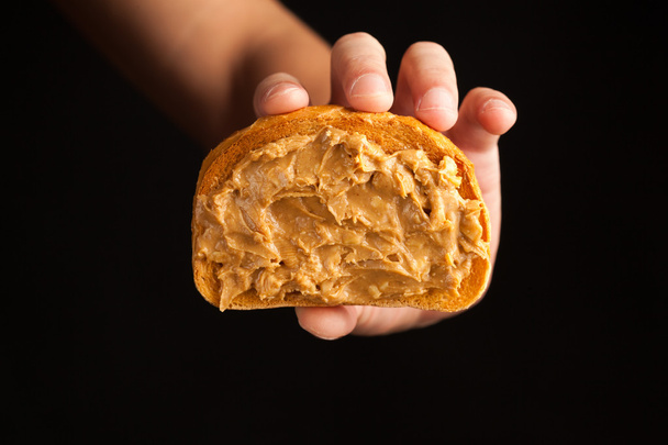黒の背景に手でピーナッツ バター トースト - 写真・画像