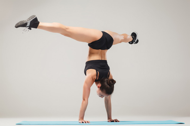 Beautiful sporty girl standing in acrobat pose or yoga asana - Fotoğraf, Görsel