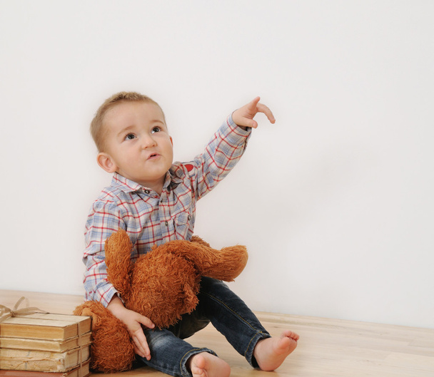 Studioaufnahme eines kleinen Jungen, der mit seinem Spielzeug und Buch mit dem Finger zeigt - Foto, Bild