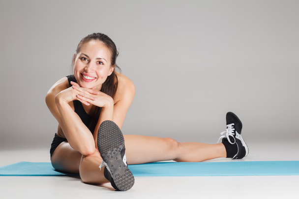 Muscular young woman athlete stretching on gray - Φωτογραφία, εικόνα