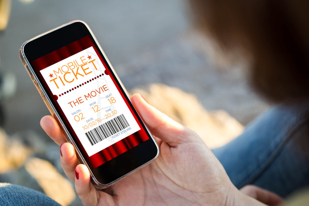 woman sitting in the street cheking a cinema e-tickets with her  - Zdjęcie, obraz