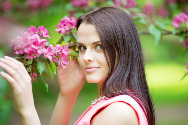 Young spring fashion woman. Trendy girl in the flowering trees in the spring summer garden. Springtime or summertime. Lady in spring landscape background. Allergic to pollen of flowers. Spring allergy - Zdjęcie, obraz