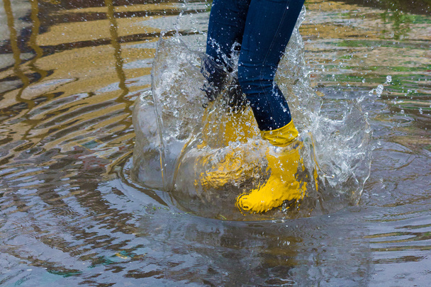 Mädchen mit Regenstiefeln springt in eine Pfütze - Foto, Bild