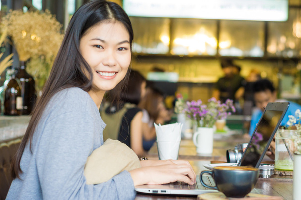 donne asiatiche sorridenti lavorano sul computer portatile al caffè, tazza di caffè
 - Foto, immagini