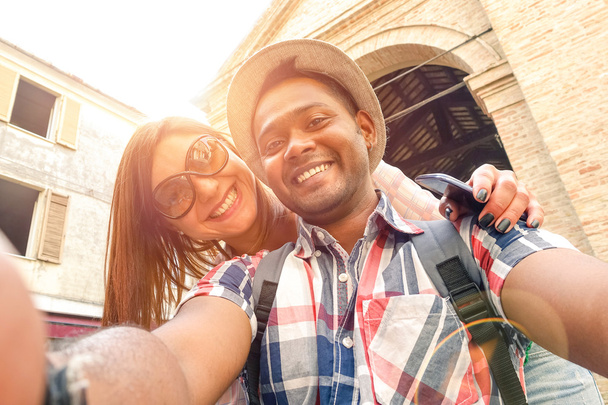 Multiracial couple taking selfie at old town trip - Fun concept with alternative fashion travelers - Indian boyfriend with caucasian girlfriend - Warm filter with powered sunlight and lens flare halo - Photo, Image