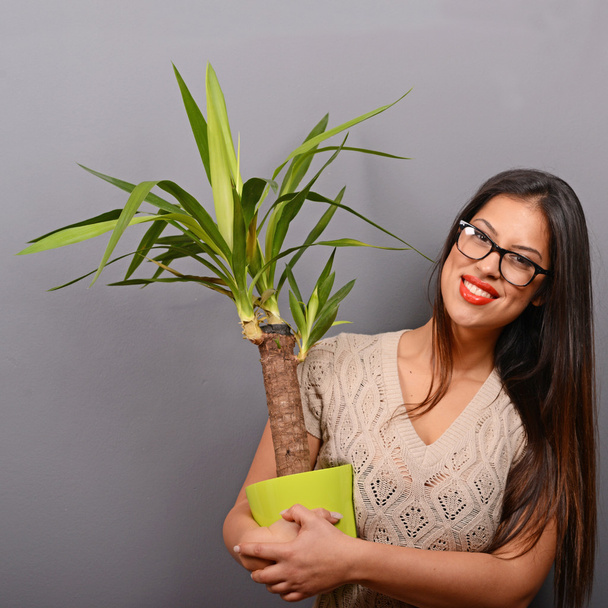 Beautiful happy woman holding plant in vase against gray backgro - Foto, Imagen