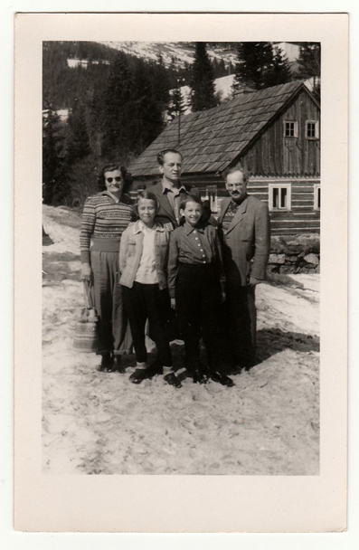 A vintage photo shows group of people In front of a log house in winter, circa 1950s. - 写真・画像