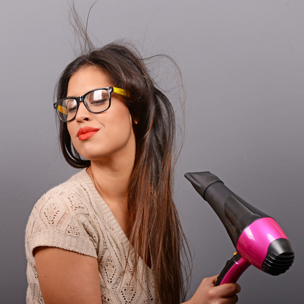 Portrait of a woman holding hair dryer against gray background - Valokuva, kuva