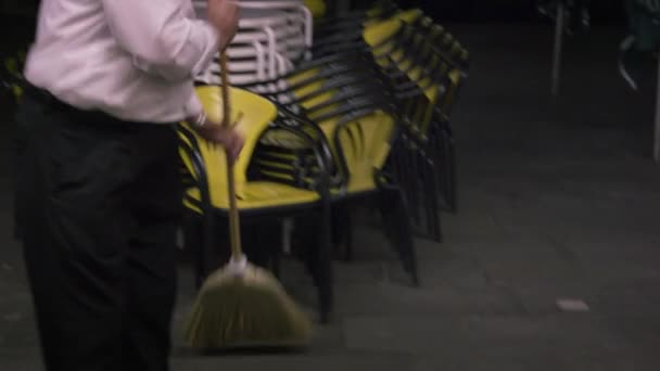 Following shot of a man sweeping up the outdoor eating area at an Italian cafe. - Кадри, відео