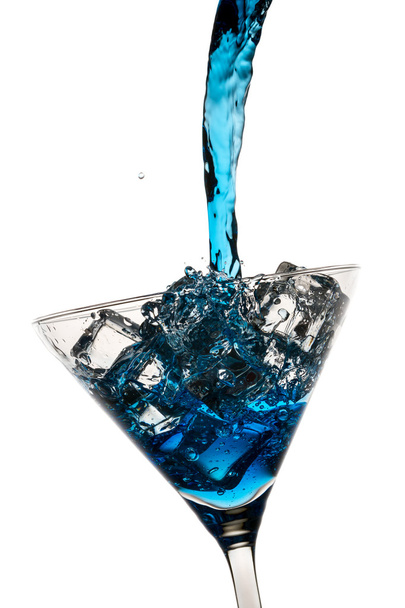 Blue liqueur poured into a martini glass with ice cubes on white - Фото, изображение