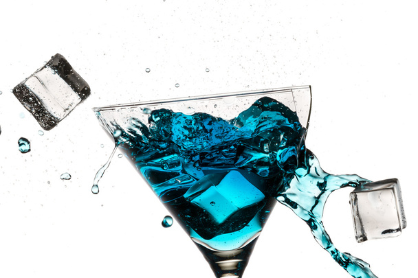 Ice cubes breaking martini glass filled with blue liqueur on whi - Фото, изображение