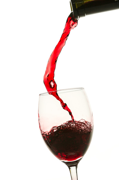 ρίχνει κόκκινο κρασί σε ποτήρι από μπουκάλι σε άσπρο φόντο - Φωτογραφία, εικόνα