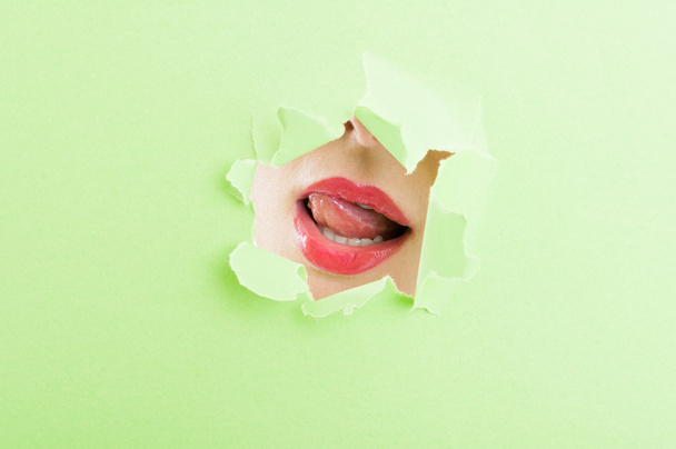 Sexy female mouth wearing lipstick thru ripped paper hole - Фото, изображение