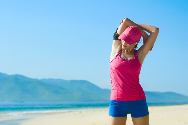 Νεαρή γυναίκα που κάνει το τέντωμα άσκηση στην παραλία. - Φωτογραφία, εικόνα