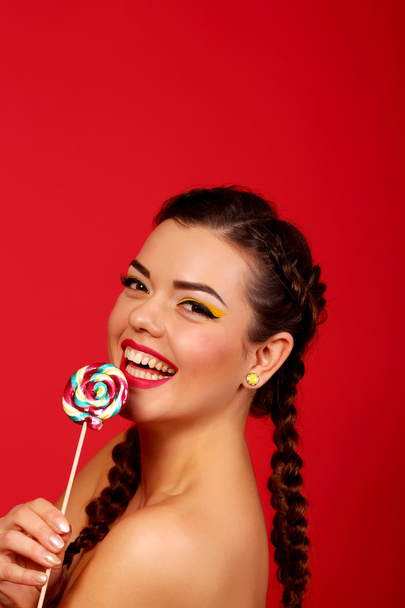 Close Up. Brunette girl with red lips, holding colorful lollipop. The beauty model portrait sweet candies on a red background. - Foto, immagini