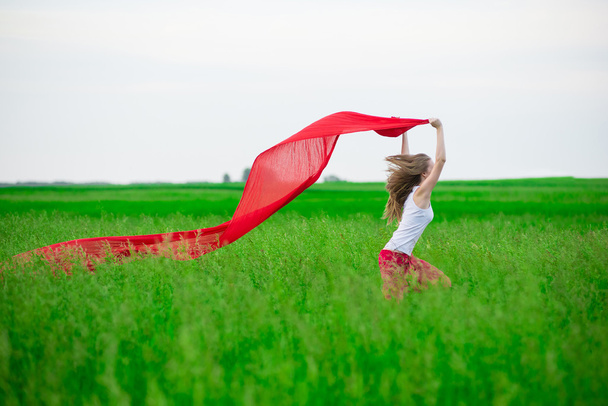 Jeune femme courant avec des tissus dans un champ vert. Femme avec écharpe
. - Photo, image