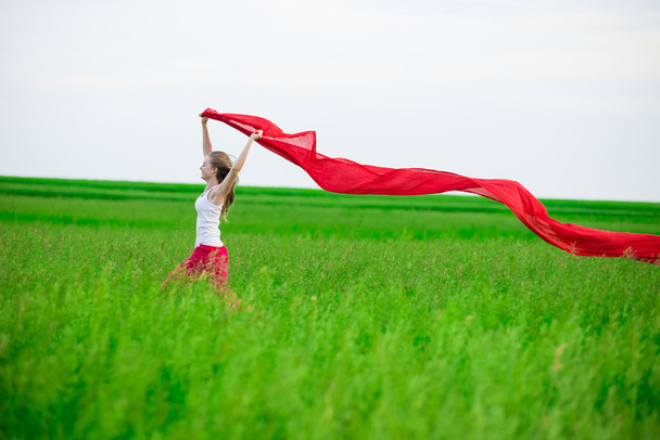 Jovencita corriendo con tejido en el campo verde. Mujer con bufanda
. - Foto, Imagen