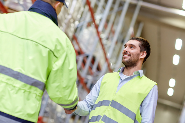 men in safety vests shaking hands at warehouse - Foto, afbeelding