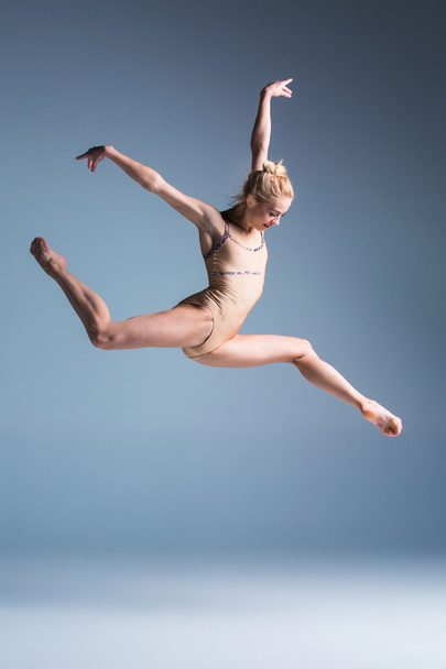 Young beautiful modern style dancer jumping on a studio background - Fotó, kép
