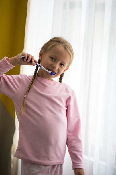 Dental hygiene. Happy little girl brushing her teeth near window - Photo, Image