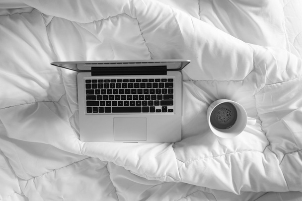 Werken in bed, laptop en wit kopje koffie op witte bed, ma - Foto, afbeelding