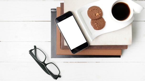 coffee cup with cookie,phone,stack of book and eyeglasses - Фото, изображение