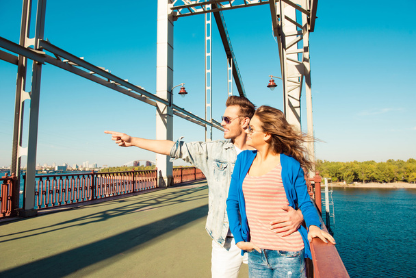 Cheerful nice couple in love on the bridge pointing away  - Fotó, kép