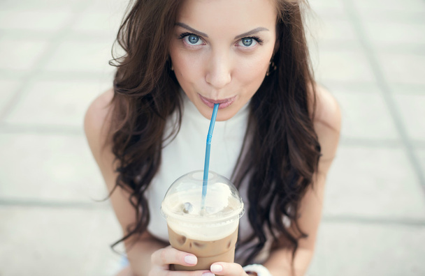 Happy beautiful girl sitting on stairs in park and drinking ice coffee - Фото, изображение