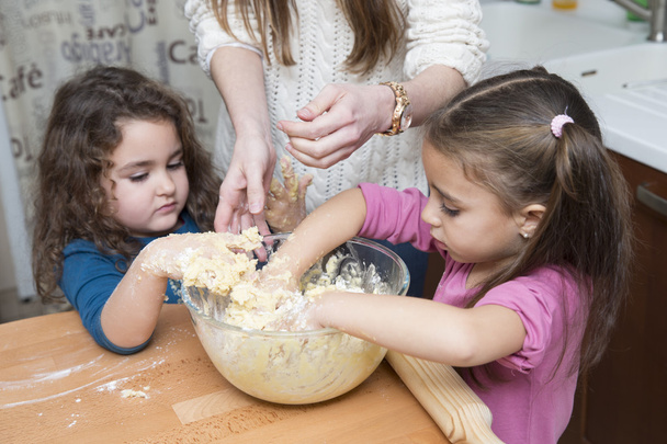 Two lovely girls and mother mixing dough with hands - Photo, image