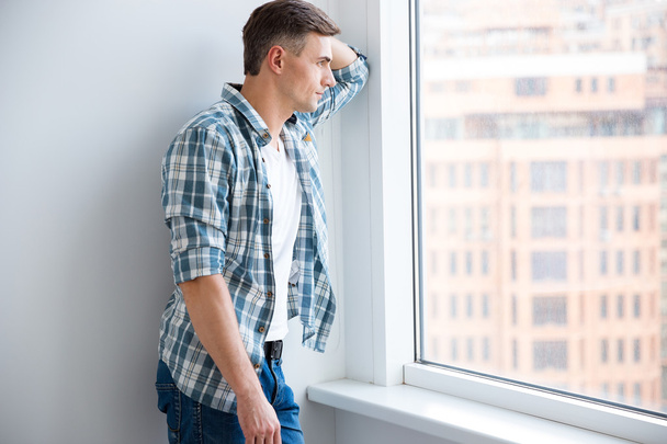 Pensive handsome man standing near the window  - Photo, Image