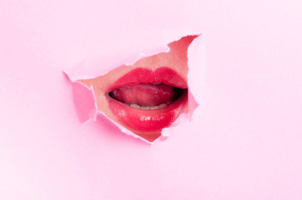 Sexy woman mouth with lipstick thru pink ripped board - Zdjęcie, obraz