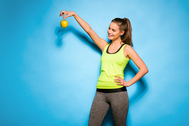 pretty woman in sport equipment holding an apple in hand - Foto, afbeelding