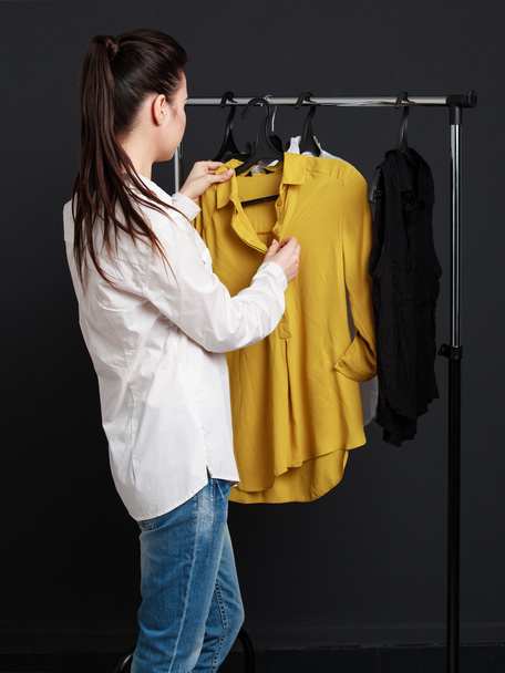 Клиент выбирает одежду. Молодая женщина в белой блузке
 - Фото, изображение