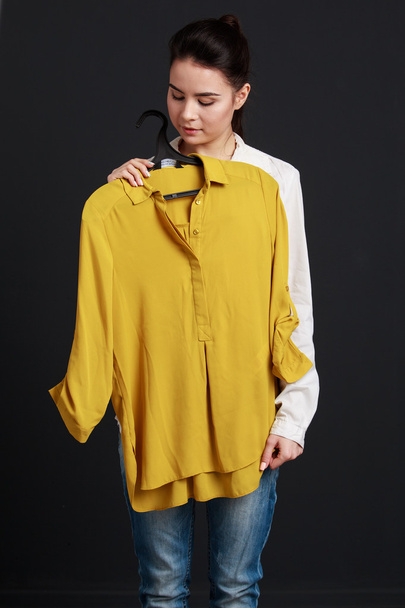 Atractiva chica morena sosteniendo una camisa amarilla y sonriendo
 - Foto, Imagen