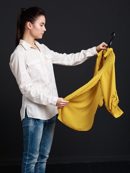 Ο πελάτης επιλέγει ρούχα σε μια μπουτίκ. Νεαρή γυναίκα σε άσπρο - Φωτογραφία, εικόνα
