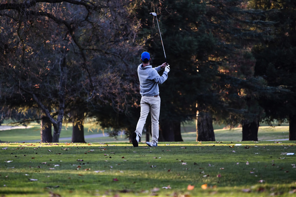 Golfer nach Schwung auf Golfplatz inmitten von Bäumen - Foto, Bild