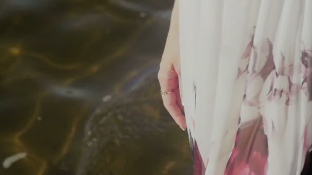 Nogi młoda kobieta w białej sukni z kwiecistym spaceru wzdłuż wybrzeża - Materiał filmowy, wideo