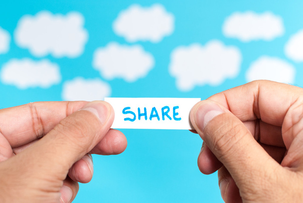 Ideen austauschen. zwei Hände halten ein Papier, das das Wort share auf blauem Hintergrund mit Wolken zeigt - Foto, Bild