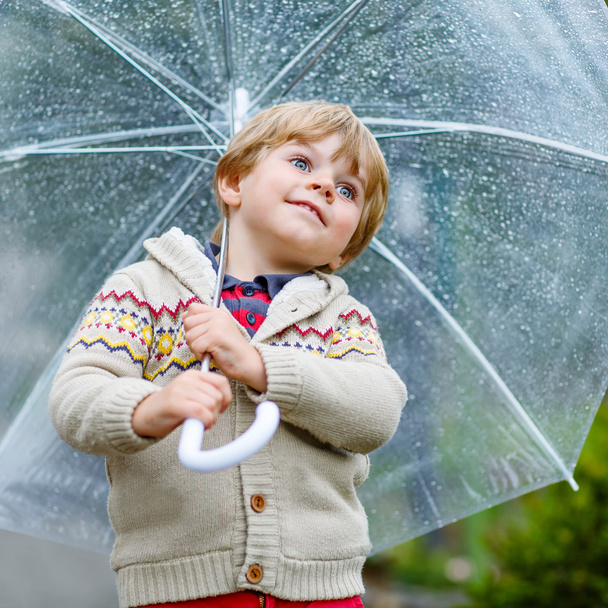 Маленький блондин, гуляющий с большим зонтиком на улице.
 - Фото, изображение