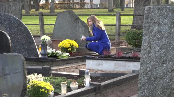 女性は、墓地に夫の父の損失の後の墓にろうそくを置きます。4 k - 映像、動画