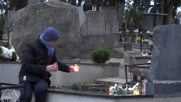 Father man put candle on daughter son grave in graveyard. 4K - Footage, Video