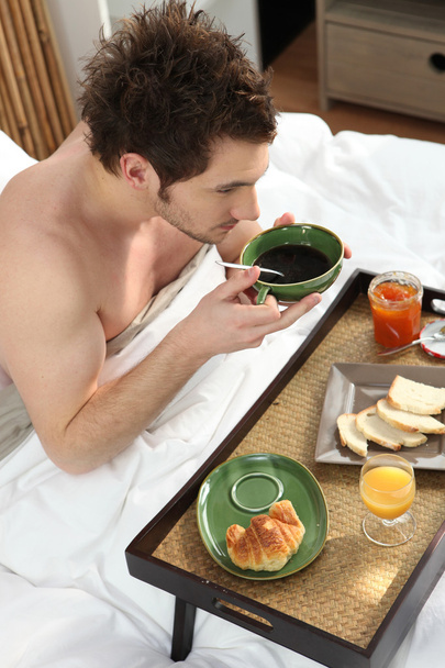 Young man having breakfast in bed - Фото, изображение