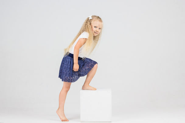 Pretty cute little blonde girl climbs white cube - Zdjęcie, obraz