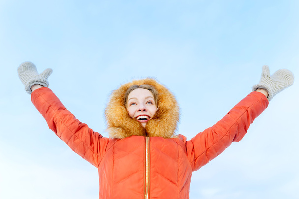 Outdoor portrait of a smiling girl in winter down jacket, raise their hands against the blue sky - Foto, imagen