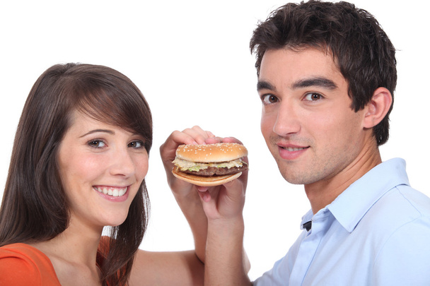Studio shot of a young couple sharing a hamburger - Foto, imagen