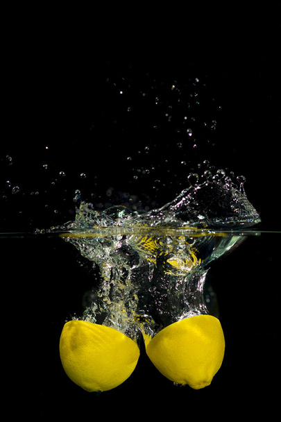 Lemon in water on black background - Фото, изображение