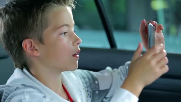Παιδί παίρνει ένα μήκος σε πόδηα με έξυπνο κινητό τηλέφωνο στο αυτοκίνητό - Πλάνα, βίντεο